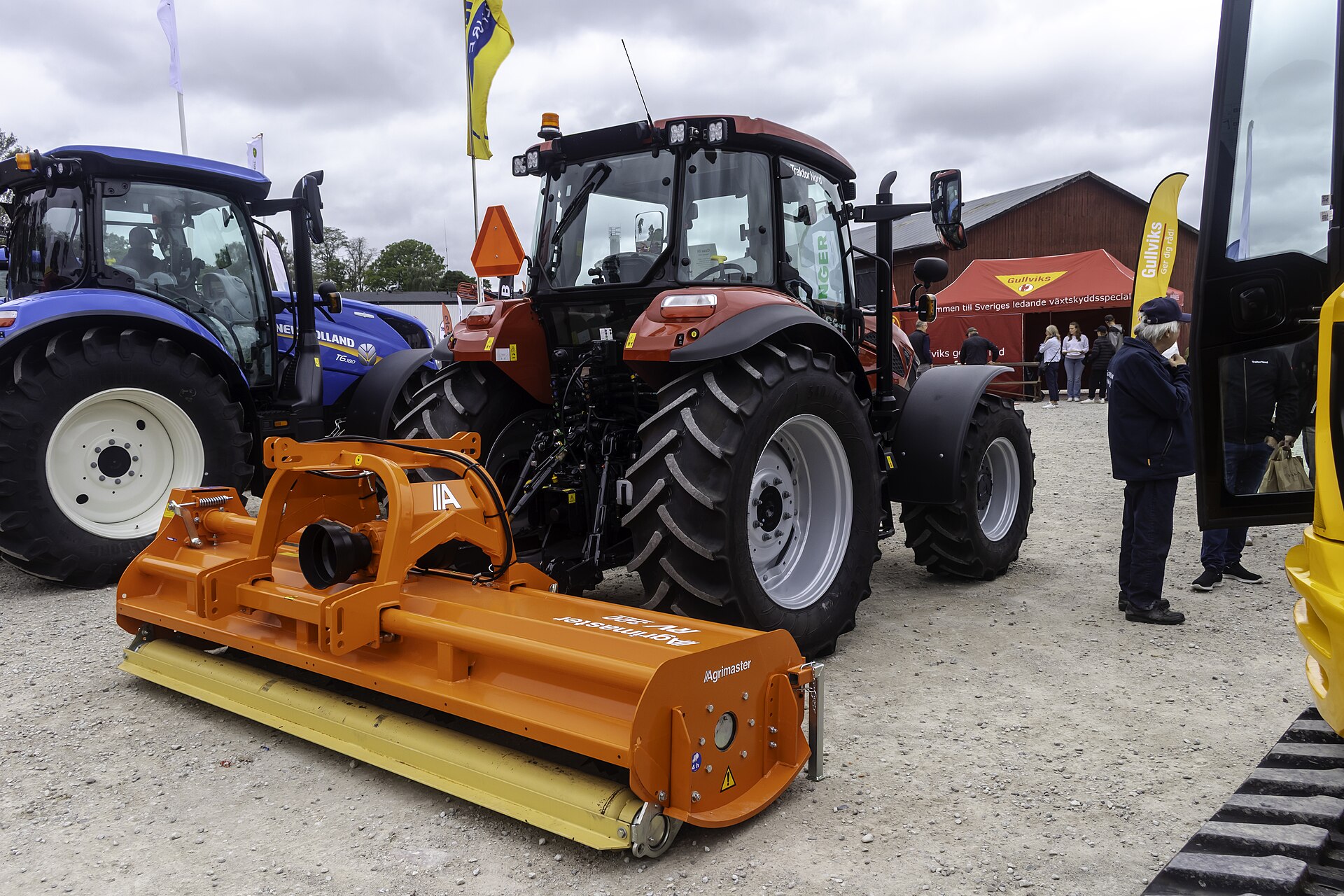 Röd Case IH-traktor sedd bakifrån med orange slagklippare på en gräsyta; modellskylten syns inte tydligt.