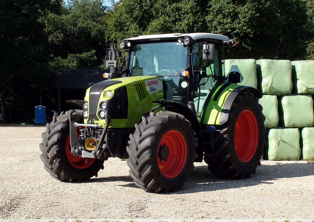 CLAAS ARION 460 med hytt, sedd snett framifrån på en grusad gårdsplan.
