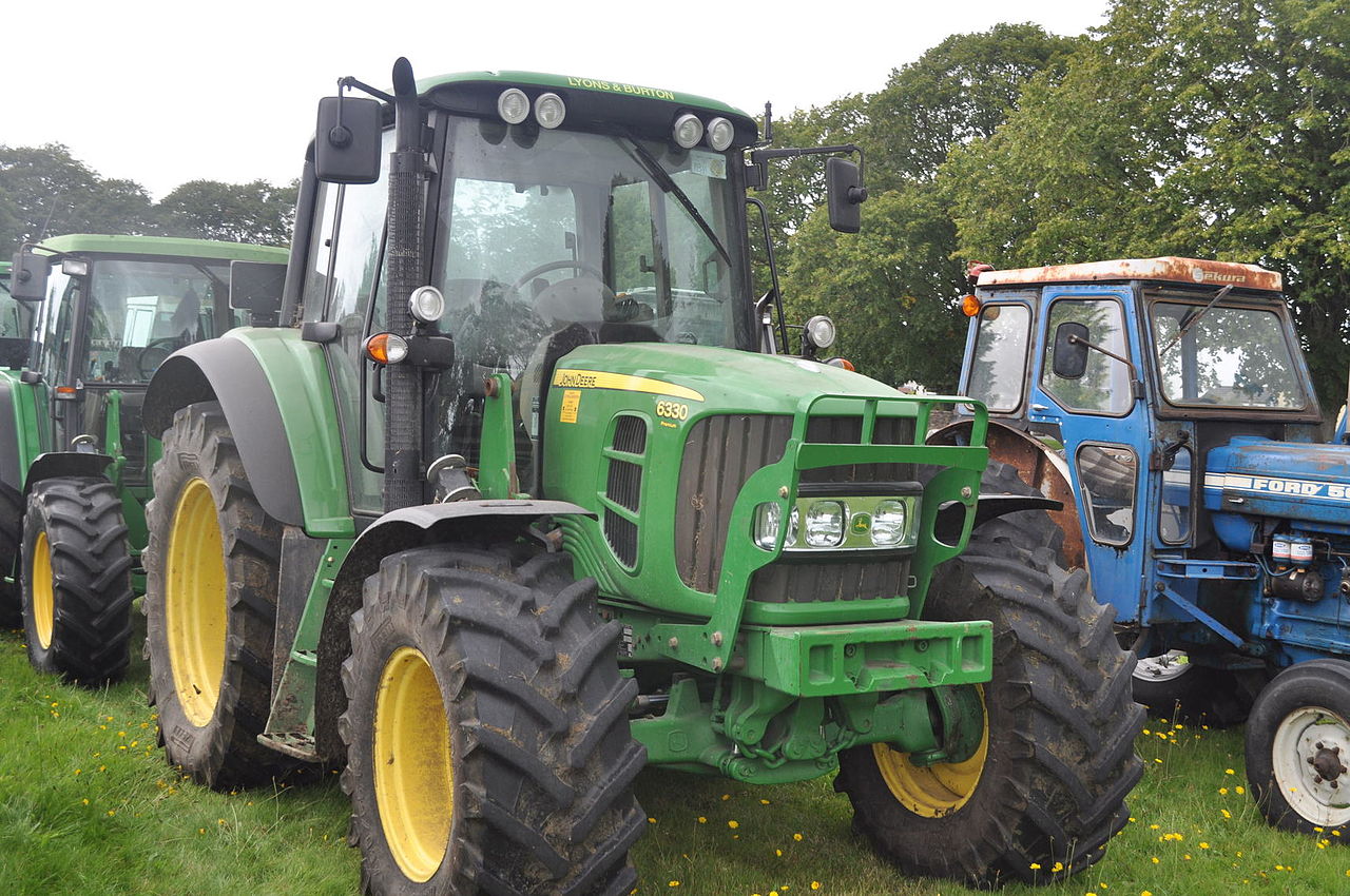 John Deere 6330 Premium vid ett traktorevenemang, med en blå Ford bredvid.