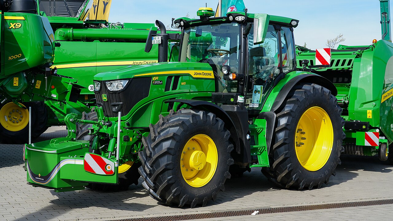 John Deere 6R 185 med en rundbalspress med inplastare på mässa.
