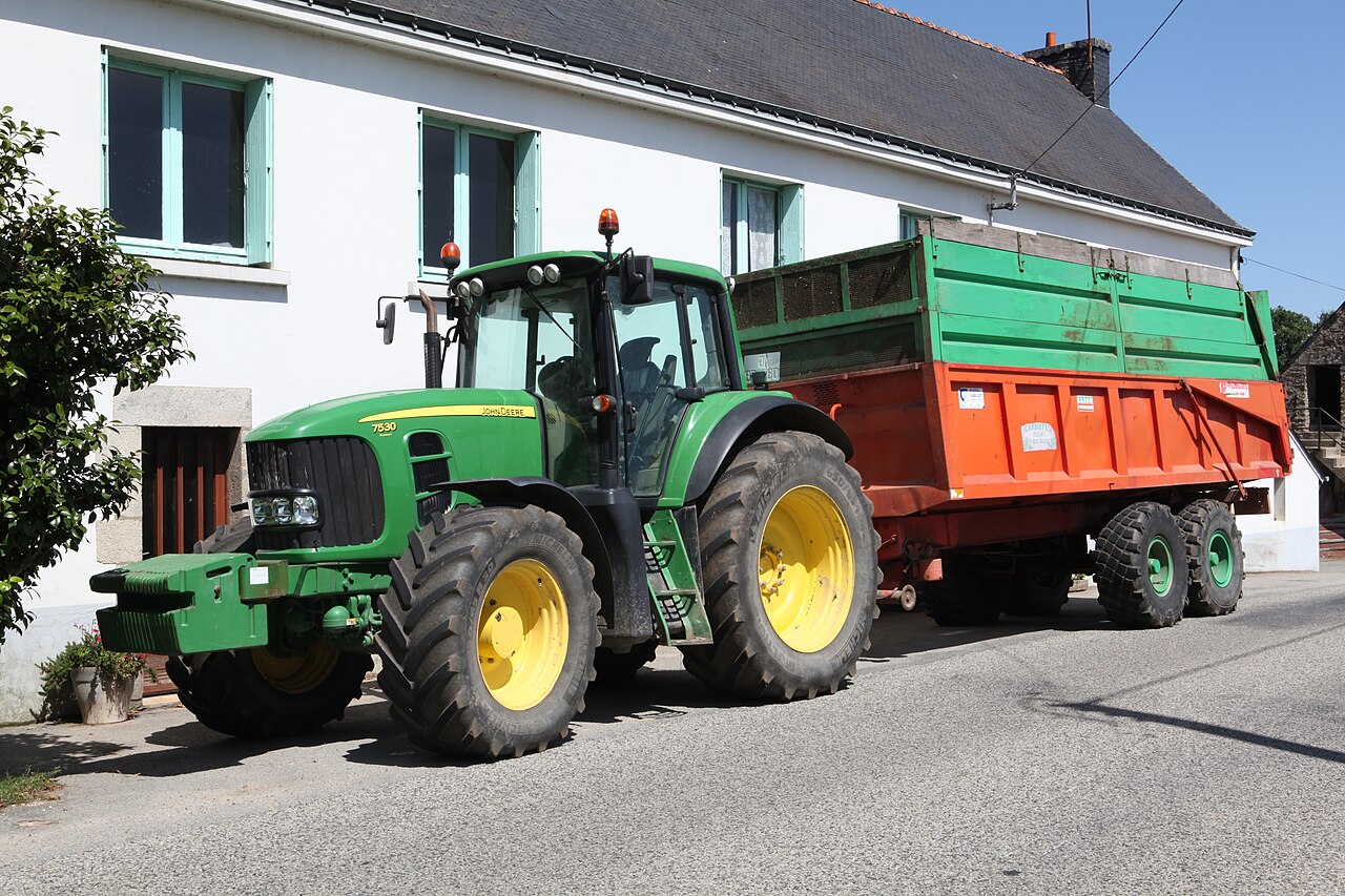 John Deere 7530 Premium med Promodis-släpvagn på en gata.