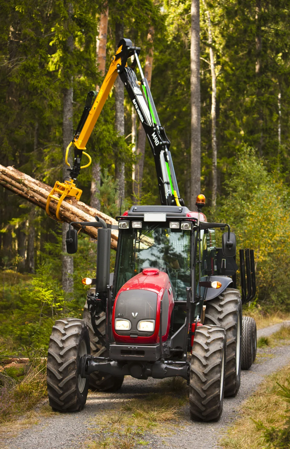 Röd Valtra A93 med skogsvagn och lastkran på en skogsväg