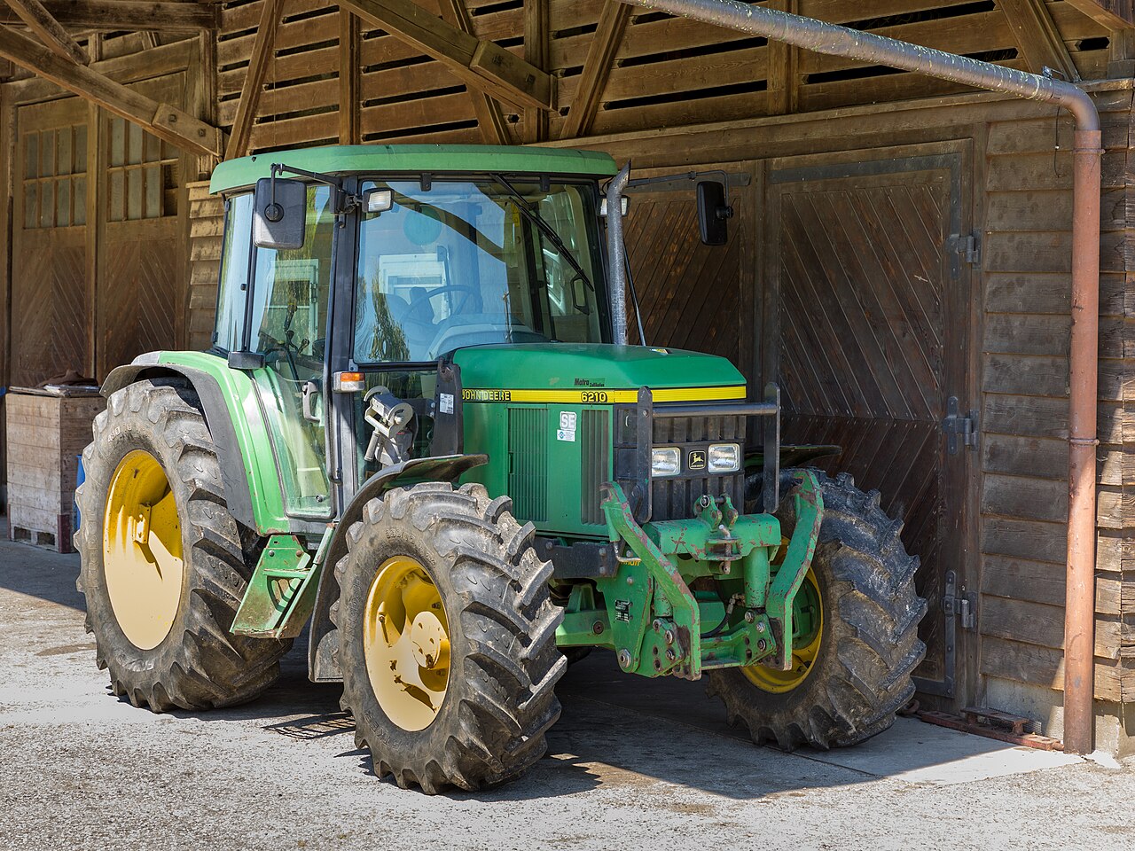 Grön John Deere 6210 SE med frontvikter, fotograferad snett framifrån vid en lada.