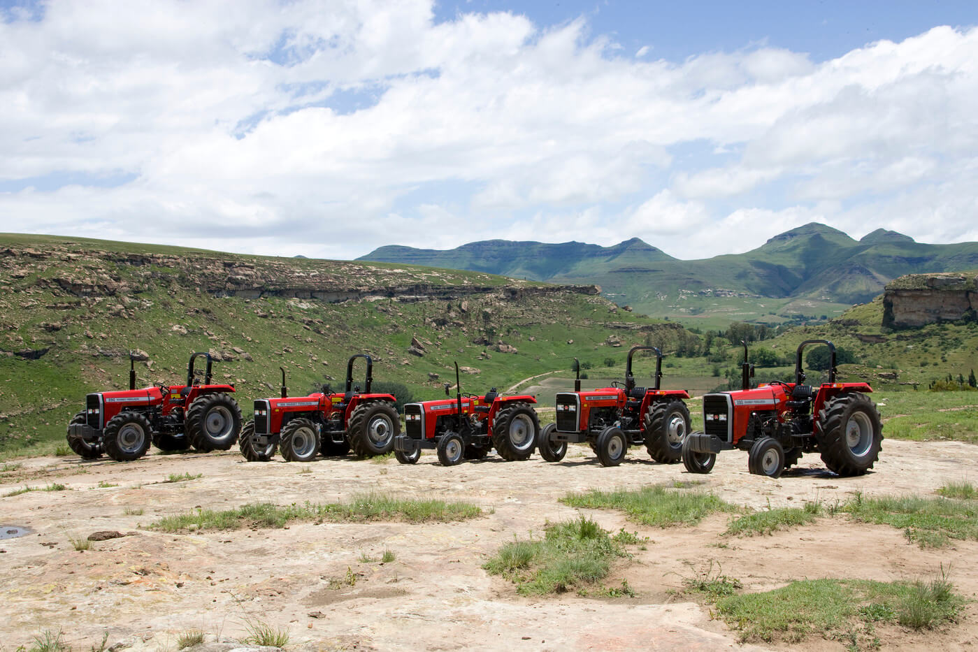 Fem röda Massey Ferguson MF 200 Xtra-traktorer uppställda i en rad i bergslandskap.