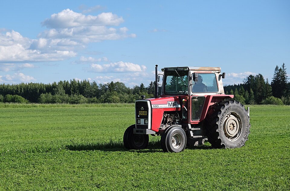 Massey Ferguson 590-traktor med bakmonterad skivslåtterkross, fotograferad snett framifrån på fält i Finland.
