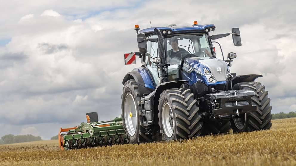 Blå New Holland T7 med standardhjulbas på ett fält; familjebild, exakt modell och transmission är inte fastställda.