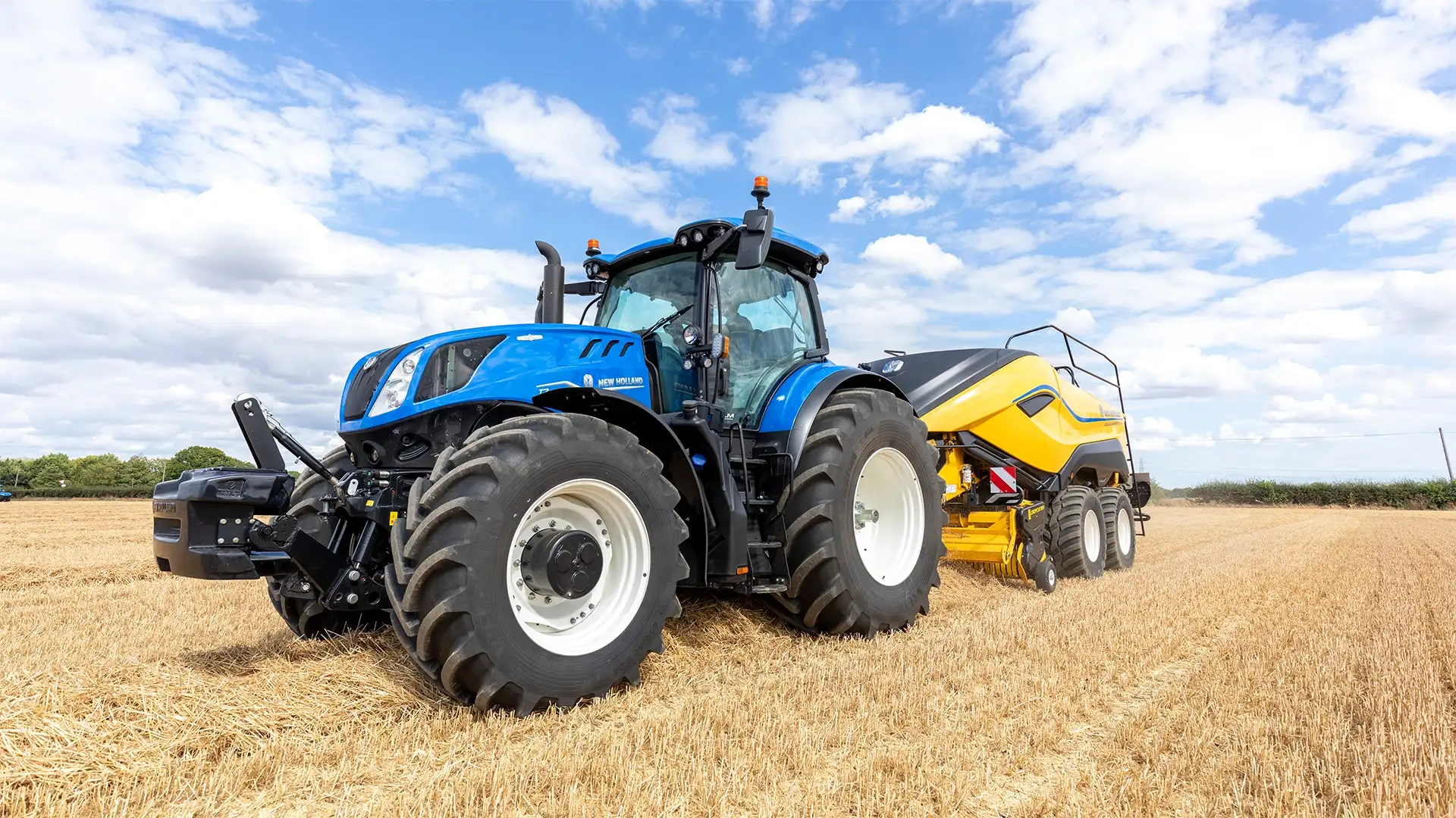 New Holland T7 Heavy Duty-traktor med balpress på ett fält; T7-modellbeteckning kan inte läsas på traktorn.