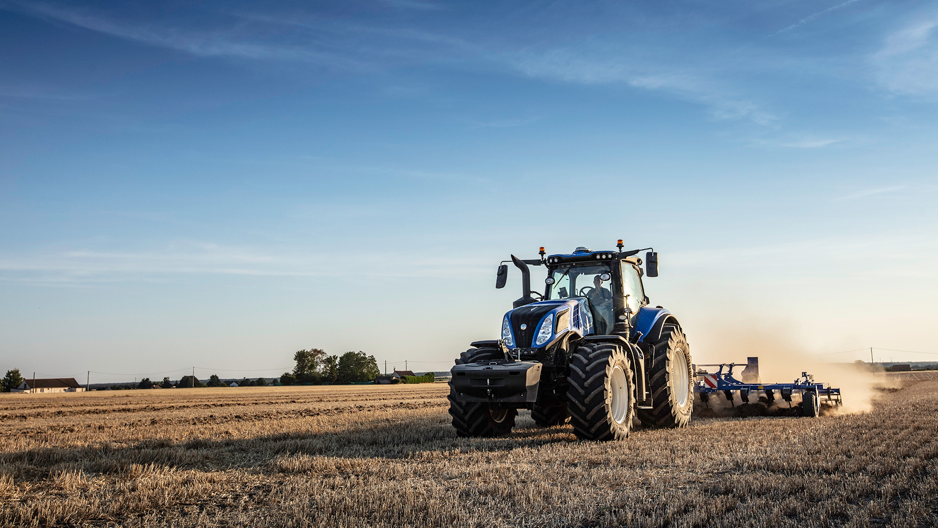 New Holland T8 Genesis med hjul och jordbearbetningsredskap på ett fält; modellfamiljebild.