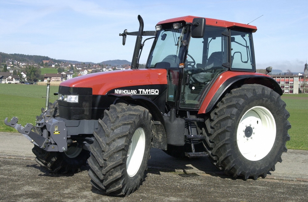 Blå New Holland TM150 från FAT:s provrapport; frontlyft och breda lantbruksdäck syns, men inte transmissionen.