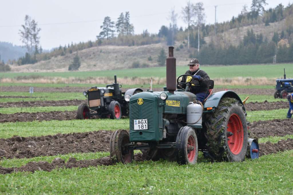 Grön Munktells BM 21 med förare på plöjd åker; modellen identifieras av Dalslands Traktormuseum.
