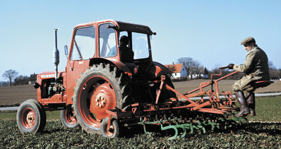 Röd Volvo BM 400 Buster med hytt och jordbearbetningsredskap på en åker.