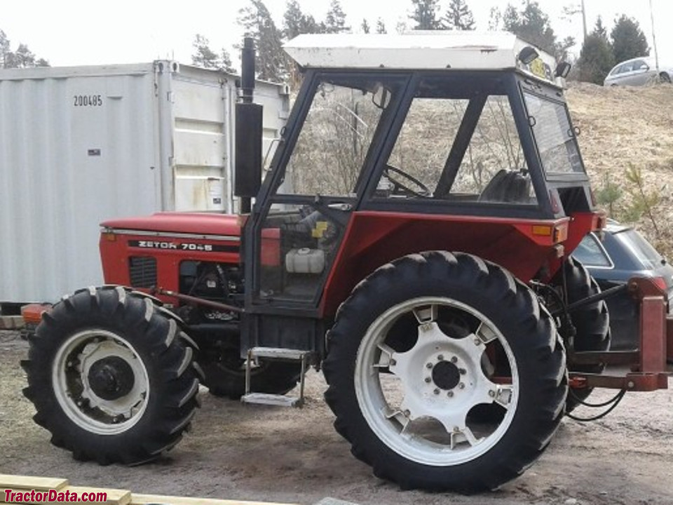 Röd Zetor 7045 sedd från sidan, med hytt och ett redskap monterat bak.